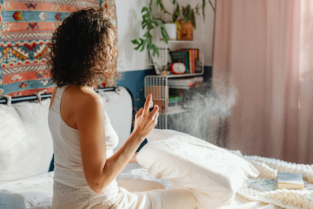 A woman spraying a room spray fragrance into the air on a bed in a bedroom