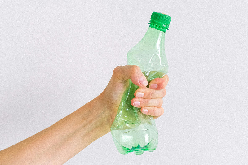 A hand squeezing an empty green plastic bottle