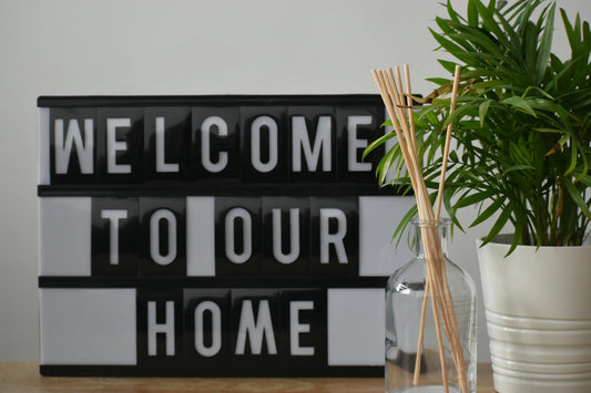 An analog marquee saying Welcome To Our Home sitting next to an oil diffuser