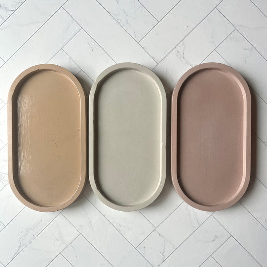A lineup of three oval tray in sand, light gray and mauve (left to right)