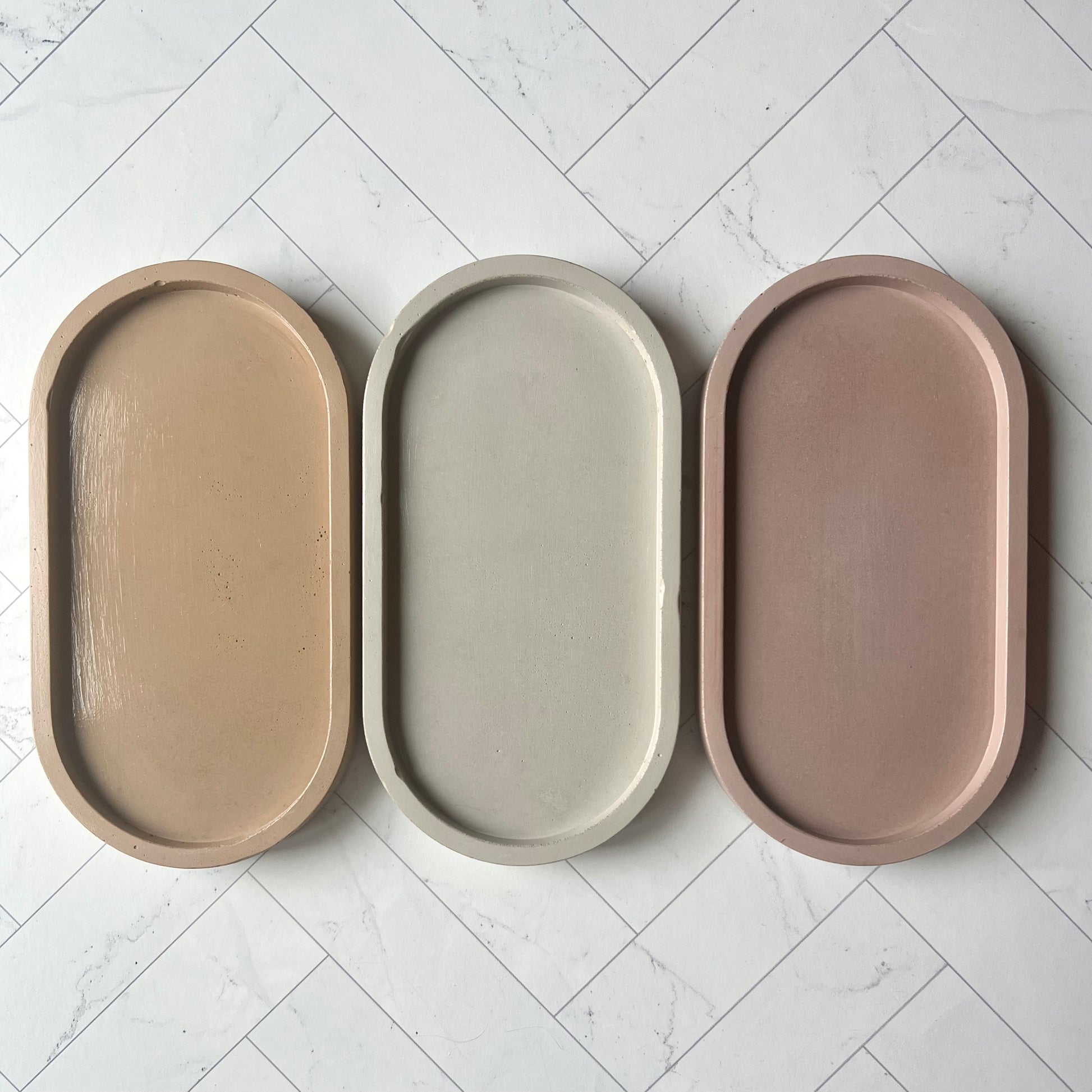 Three oval trays lined up side by side in different colors, the sand one on the left then light gray and then the mauve tray on the right