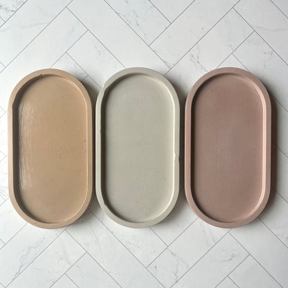 Three oval trays lined up side by side in different colors, the sand one on the left then light gray and then the mauve tray on the right