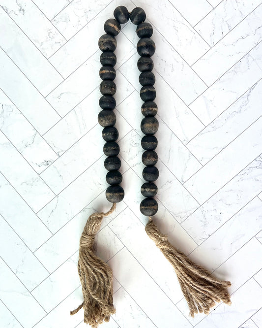 A strand of black beads with jute tassels against a while tiled background