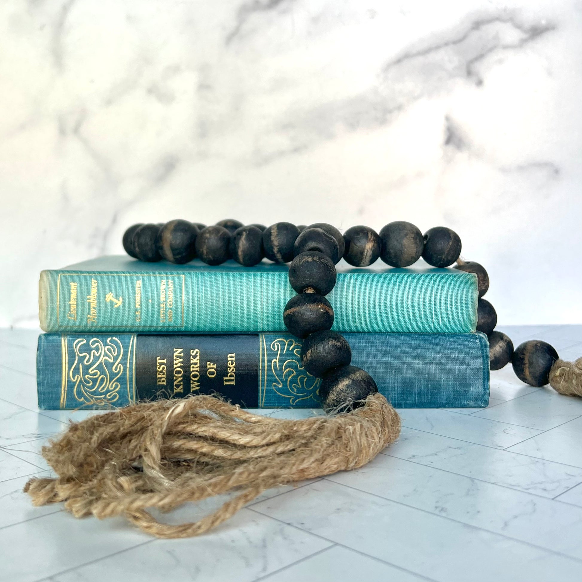 A black bead garland with jute tassels on top of two old blue books with a white marble background