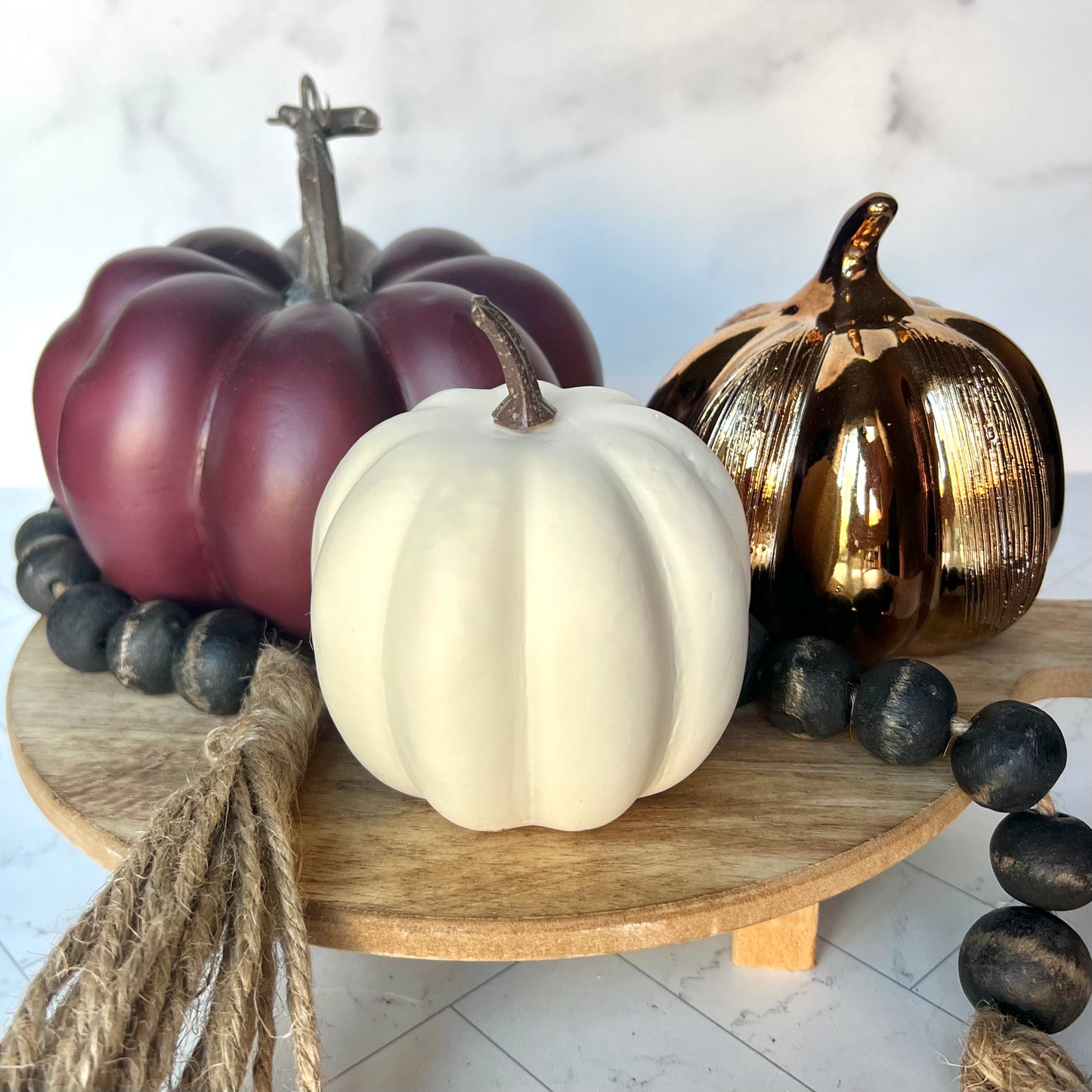 A white, copper, and purple mini pumpkin on a wooden riser with a black bead garland woven throughout the pumpkins