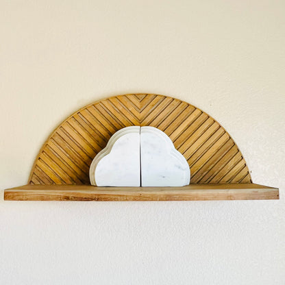 A set of white marble bookends in the subtle shape of clouds sitting on a natural wood starburst-shaped shelf