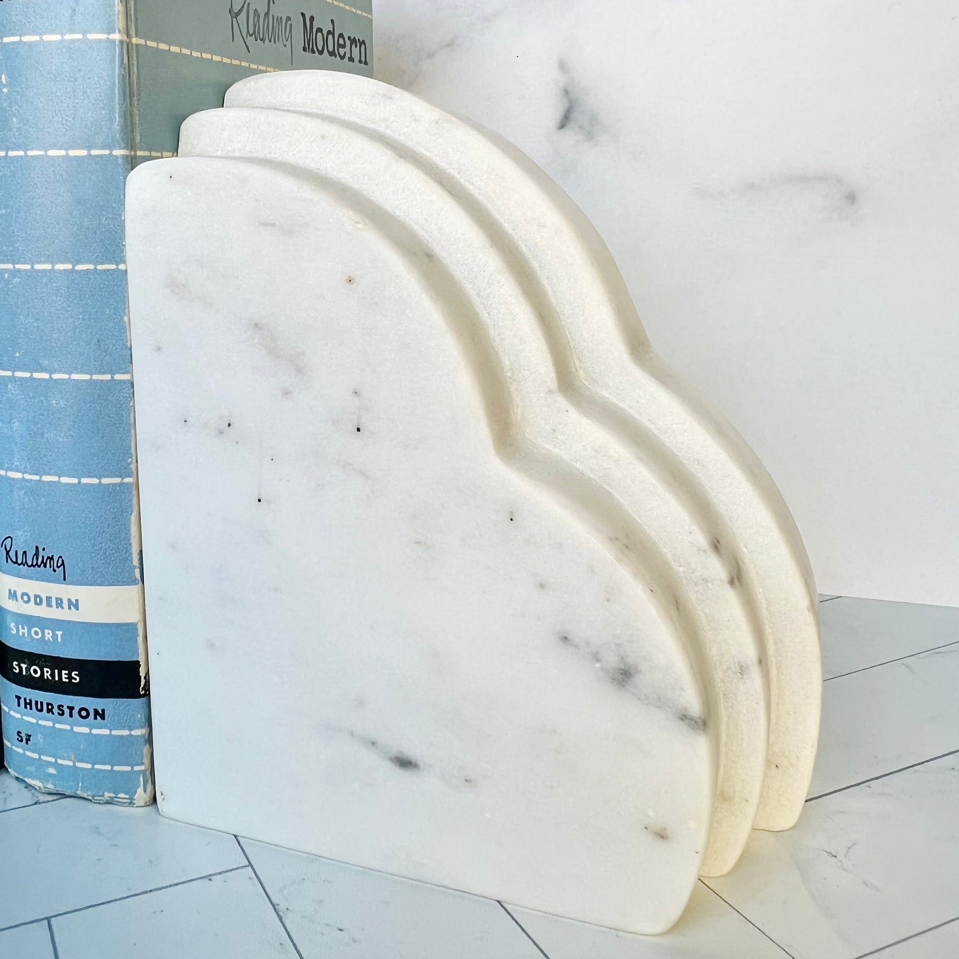 One white marble bookend shaped like a cloud with a three-tiered edge holding up a blue book