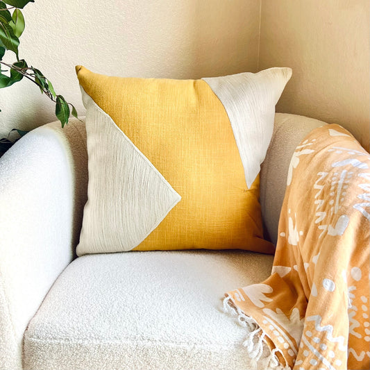 The Handmade Ochre Colorblock Throw Pillow on a white chair with an orange throw blanket on the arm - The Offbeat Co.