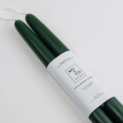 A close up of two dark green taper candles with a white label wrapped around them