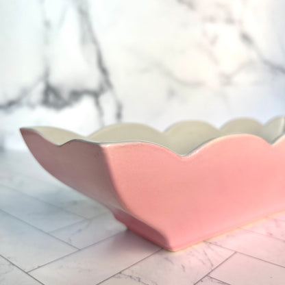 A corner of a pink scalloped-edge dish shown on a white tiled surface