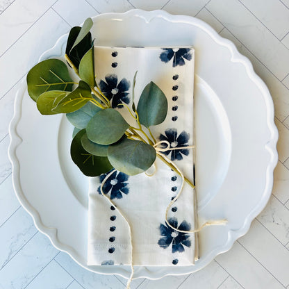 A floral block print napkin, folded atop a white plate with a sprig of greenery on top