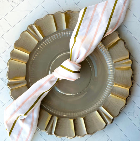 A knotted Candy Stripe Cloth Napkin set on a plate charger