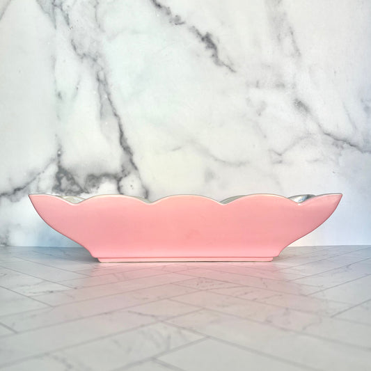A wide, short pink planter on a white tiled surface against a white marble background
