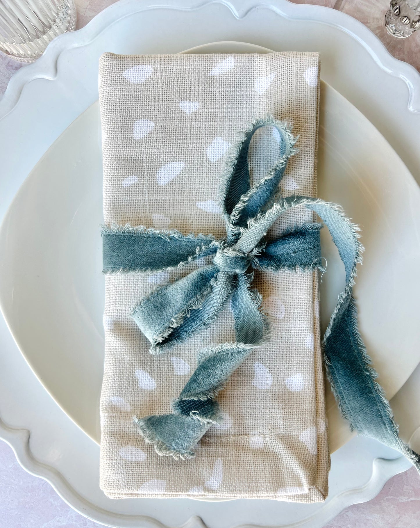 A close up of a folded Fawn Print Napkin shown overhead wrapped in blue velvet ribbon