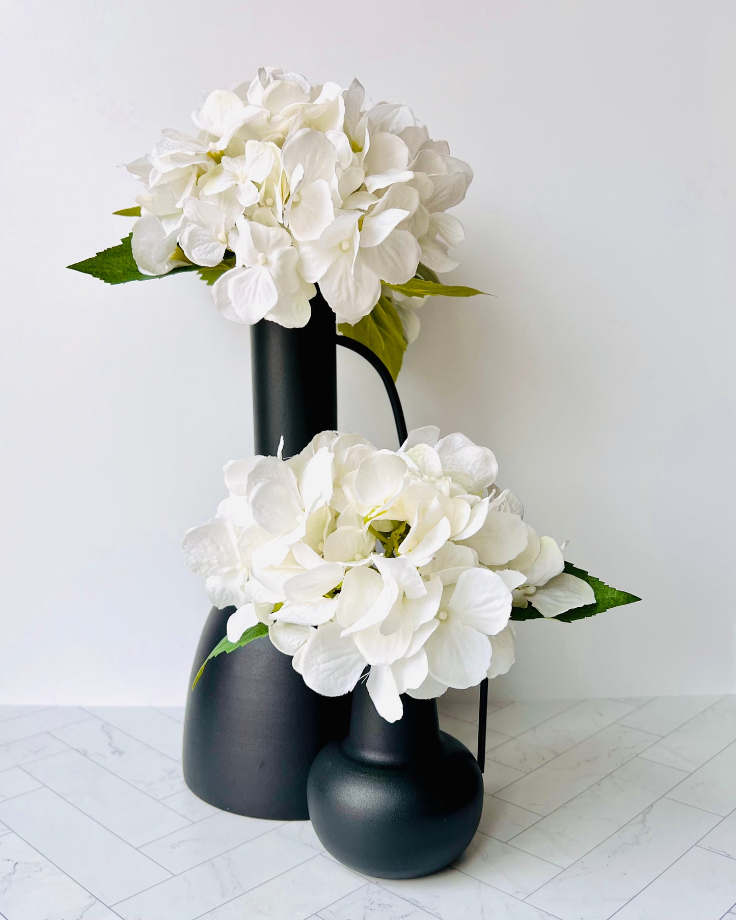 The Sleek Black Vase behind the Sleek Bud Vase both filled with white flowers