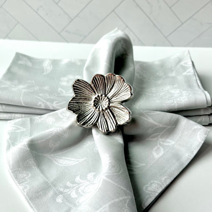 A Gray Floral Napkin with a silver flower napkin ring around it