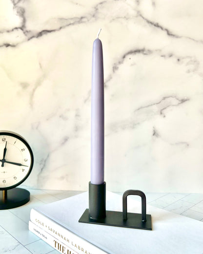 The Lucian Taper Candlestick on a table with a clock in the background - The Offbeat Co.