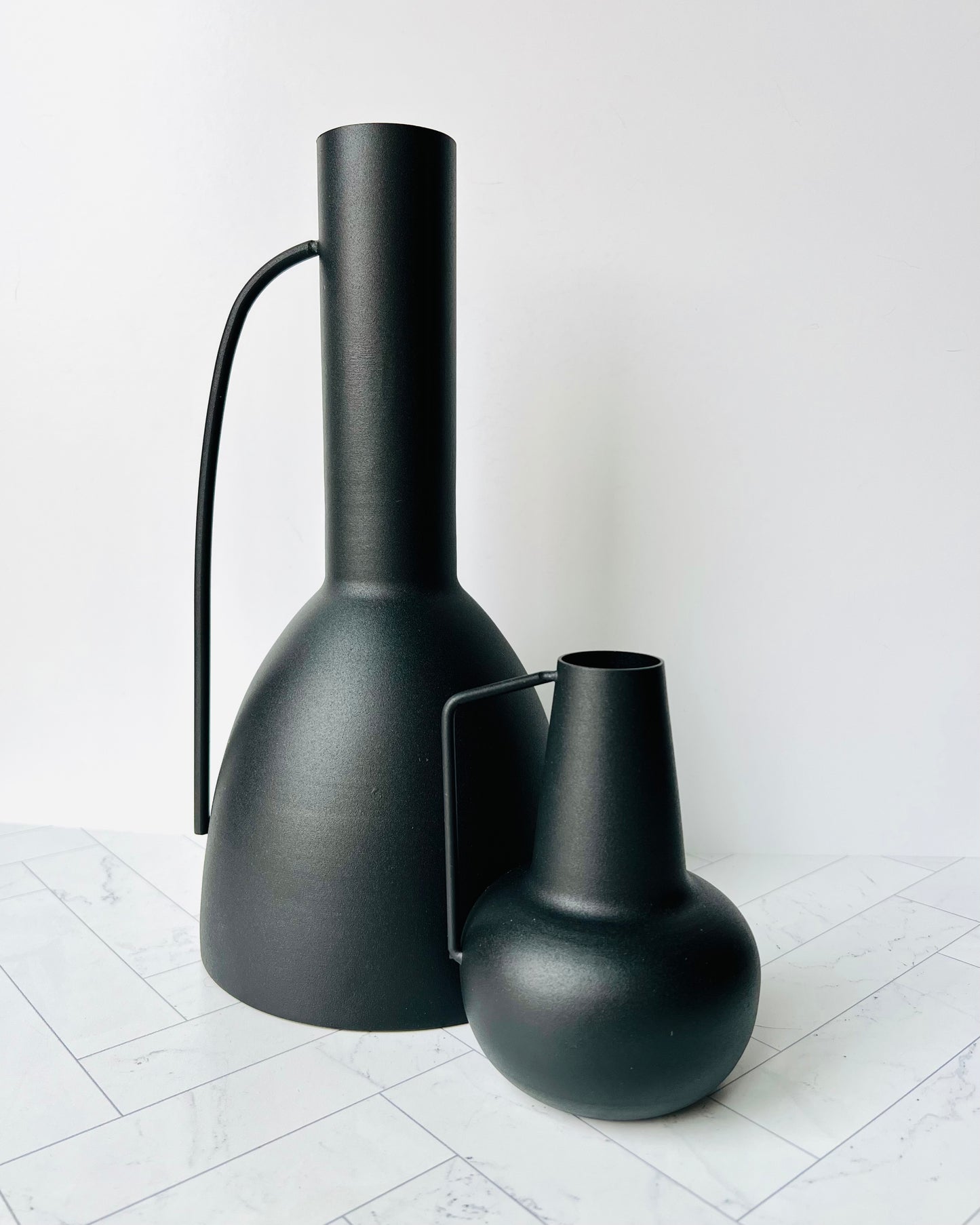 The Sleek Bud Vase sitting on a white tiled surface next to the larger Sleek Metal Vase