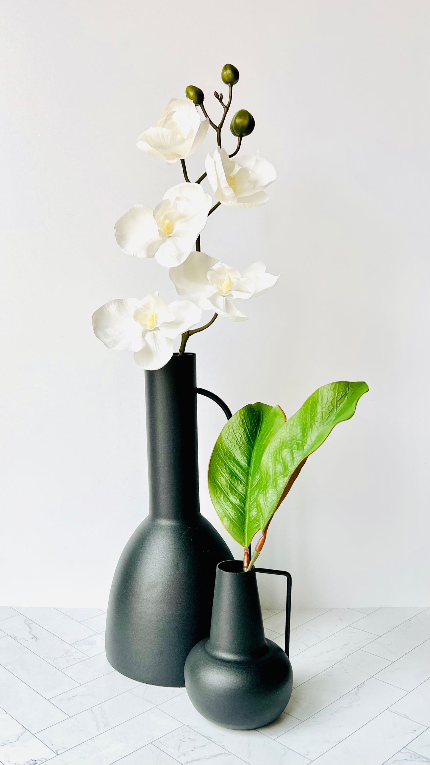 A small black bud vase and larger black vase filled with greenery and flowers, respectively