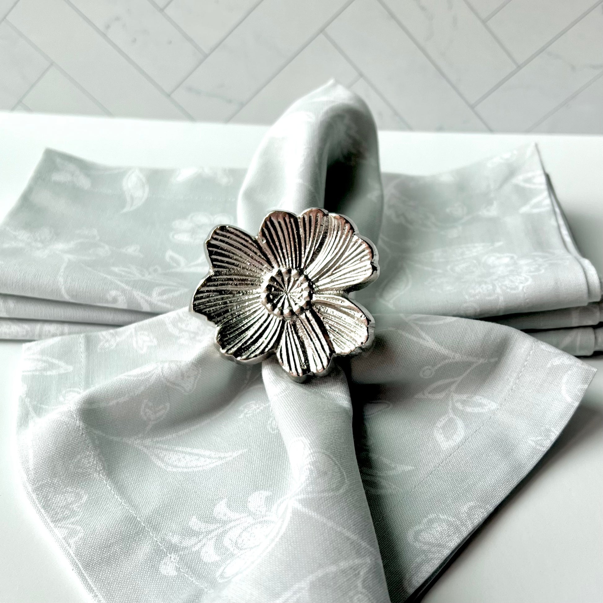 A silver flower napkin ring wrapped around a light gray napkin on a table