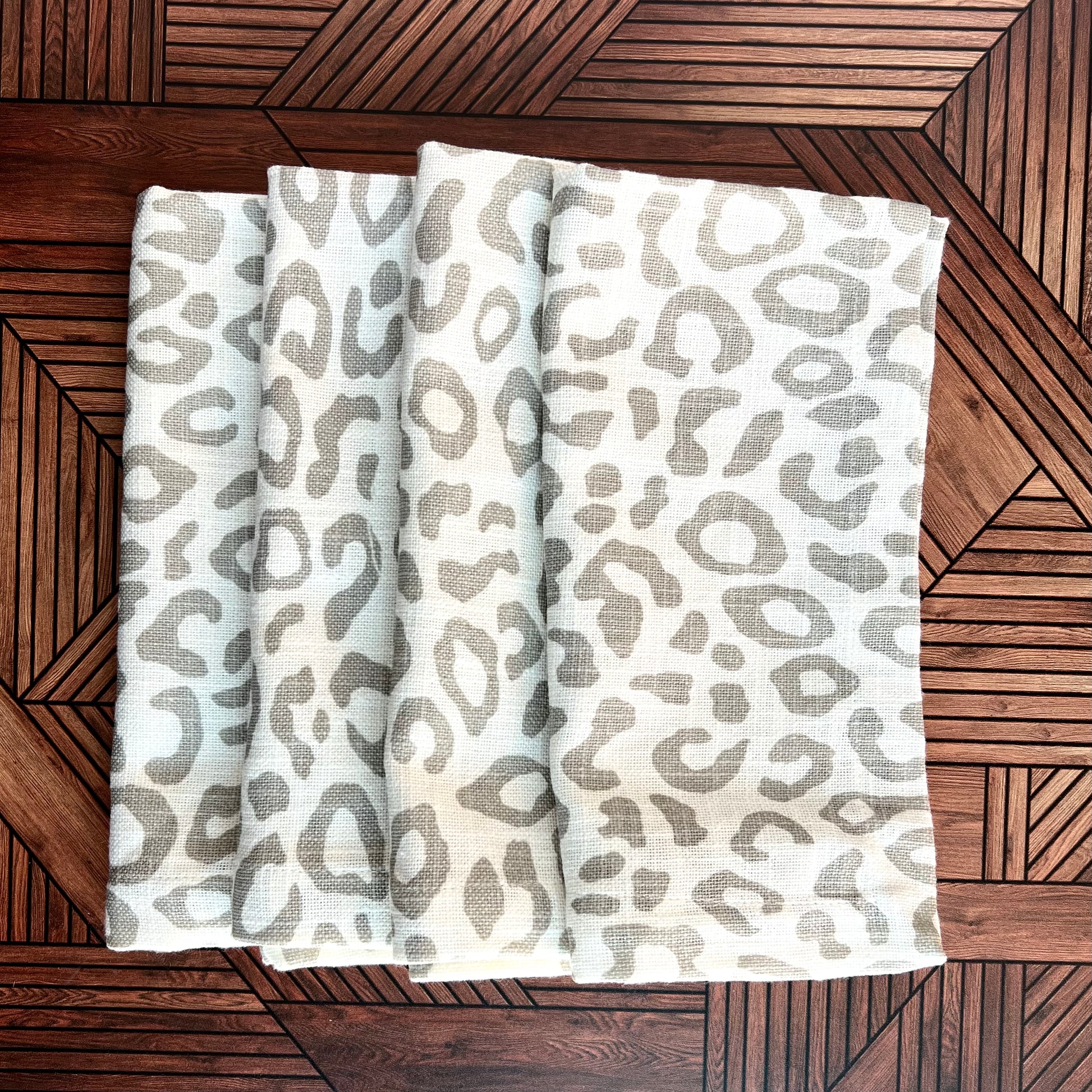A set of four leopard print napkins stacked in an array against a brown wooden background