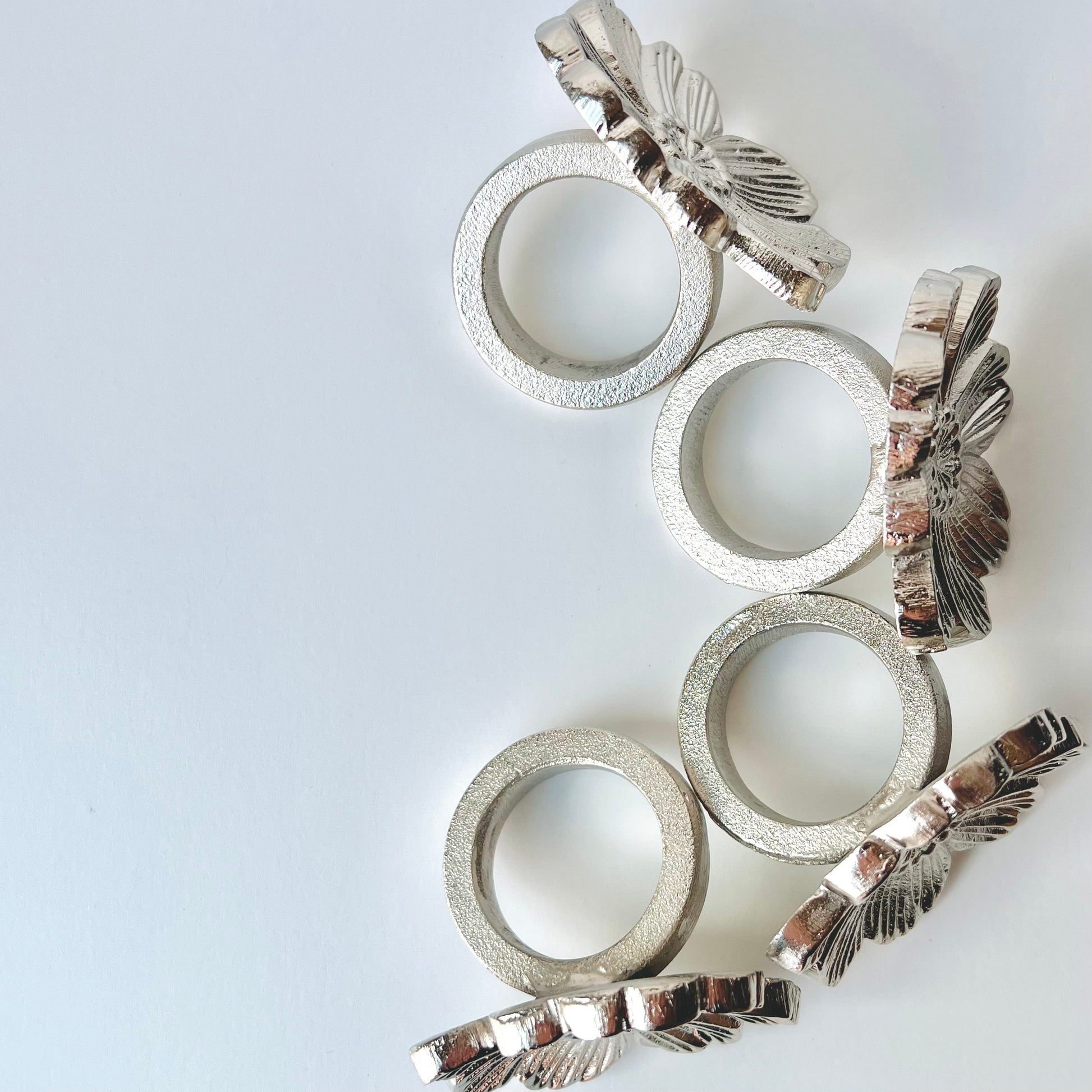 A set of four silver flower napkin rings shown from overhead to show their rings and front decorations