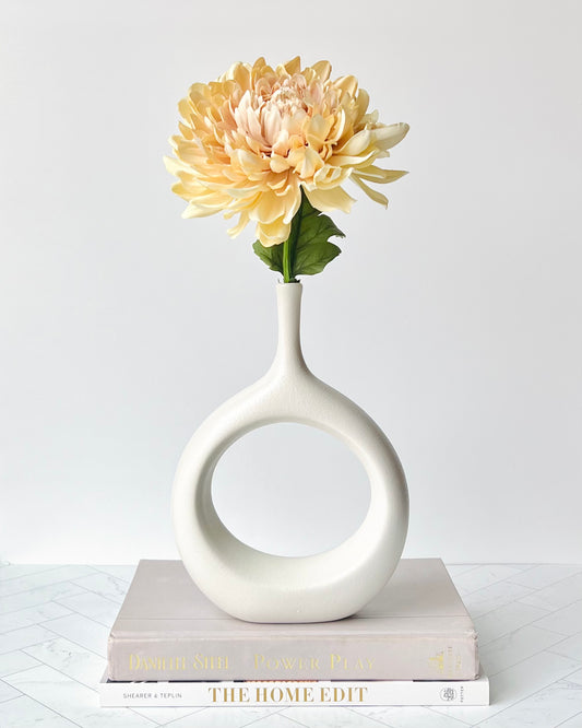 The Hollow Round Vase filled with a peach-colored flower and set atop a stack of books