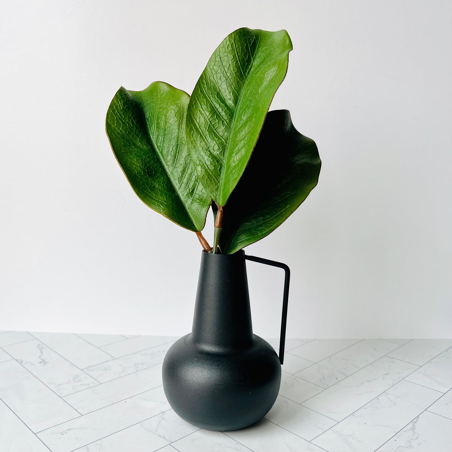 A small black bud vase filled with a few magnolia leaves