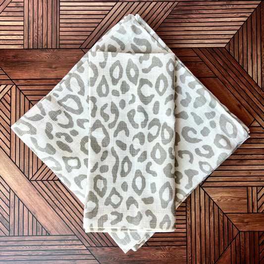 A Leopard Print Napkin folded in a rectangle on top of other leopard napkins in the shape of a square against a wooden surface - The Offbeat Co.
