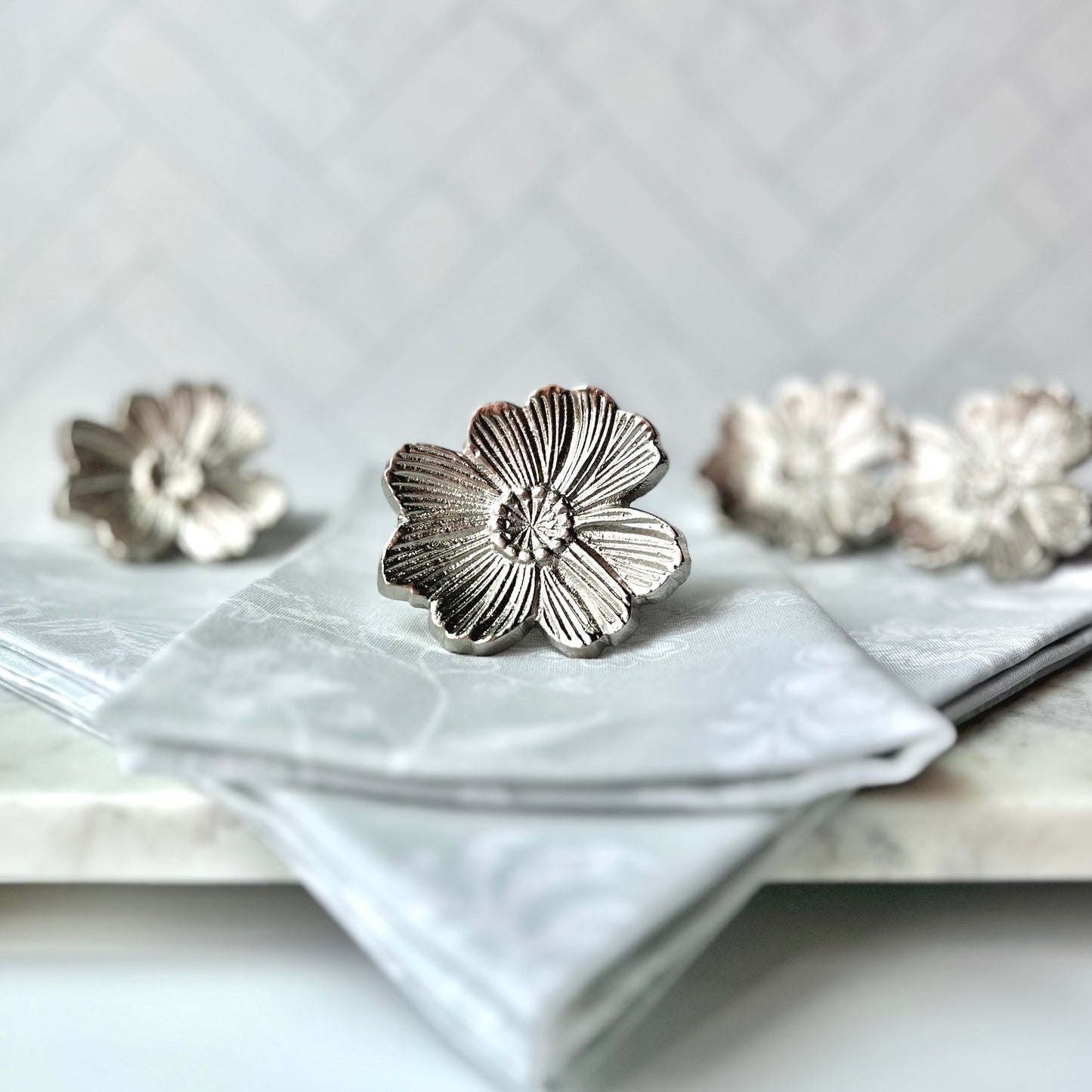 The Gray Floral Napkins shown inset with silver flower napkin rings set on top and in the background