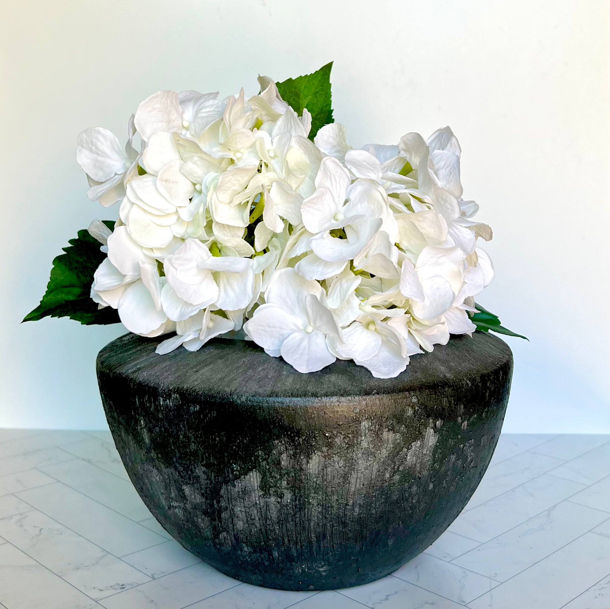 A Patina Planter on a white surfacefilled with white hydrangea blossoms