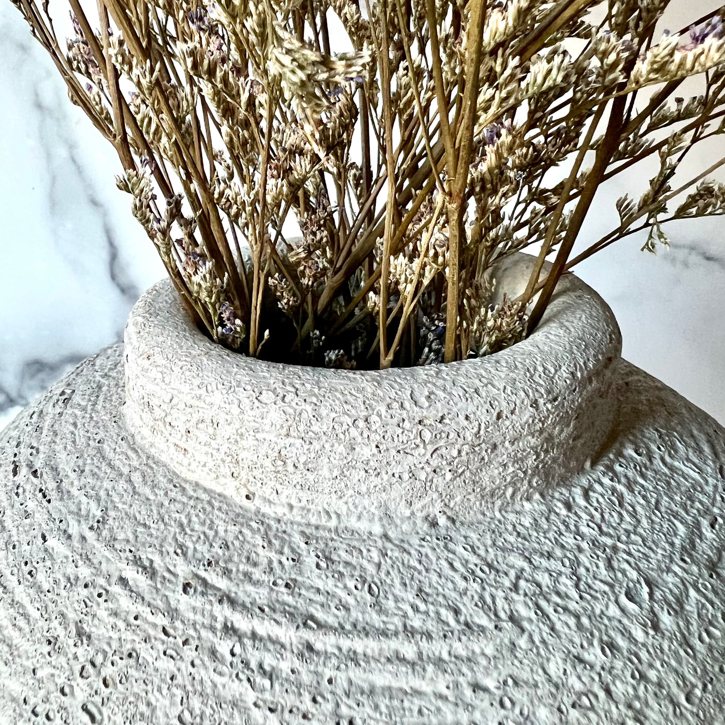 The above-angle view of a the opening of a gray vase filled with dried flowers