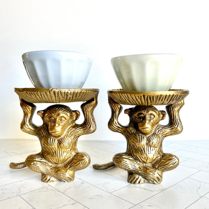 Two brass monkey figurines shown with small condiment dishes on their pedestals
