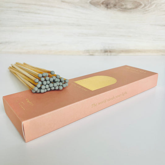 A light pink matchbox with a bundle of gray-tipped matches resting on top at an angle
