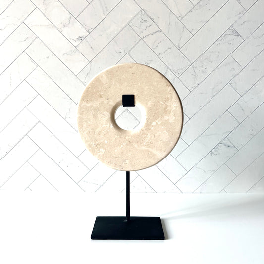 A standing beige marble disc on a black stand against a light background