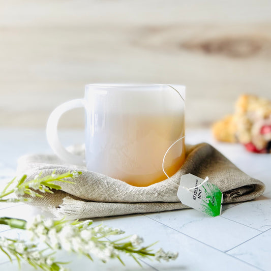 One White Glass Mug filled with tea and set on a beige cloth napkin