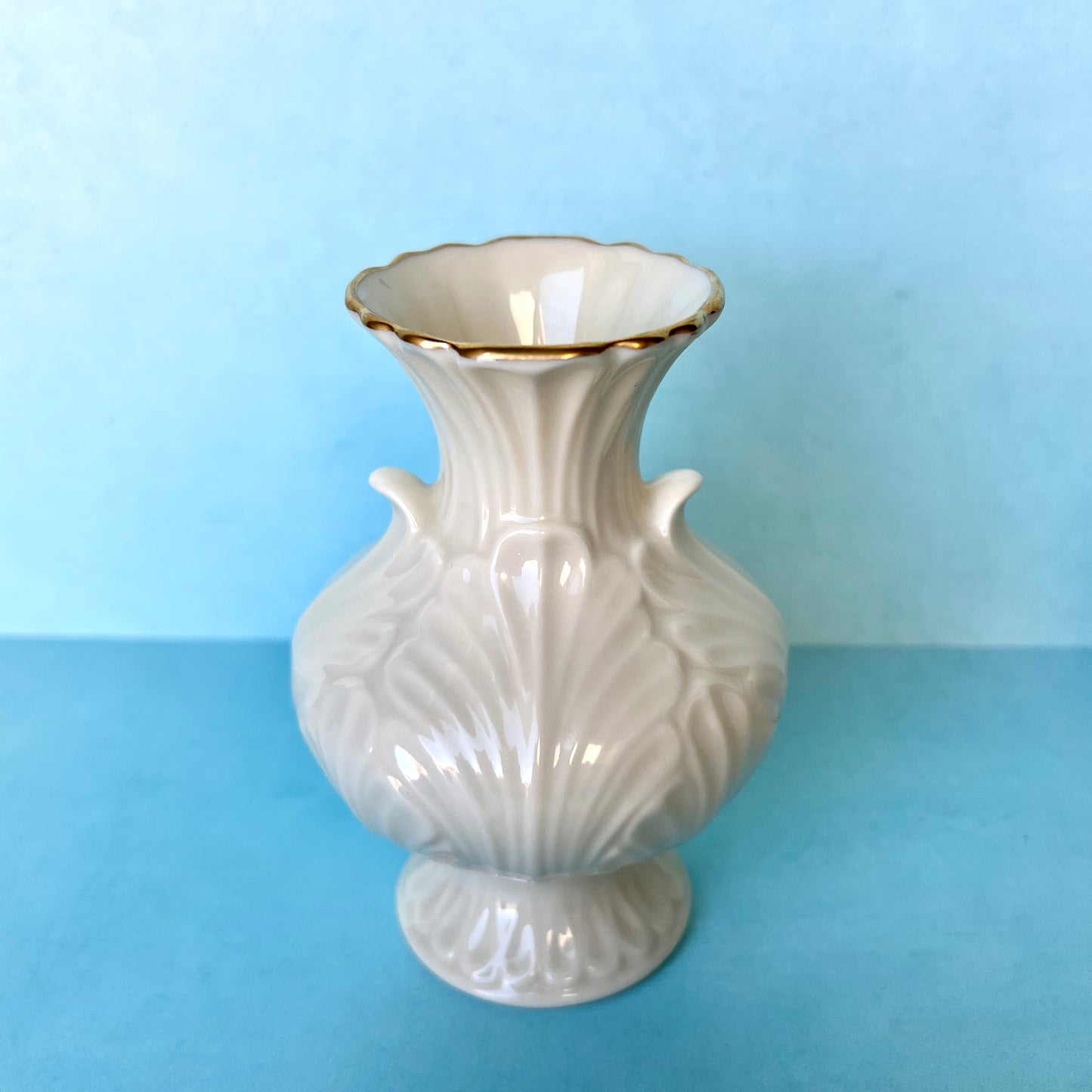 A white bud vase with gold trim against a blue background
