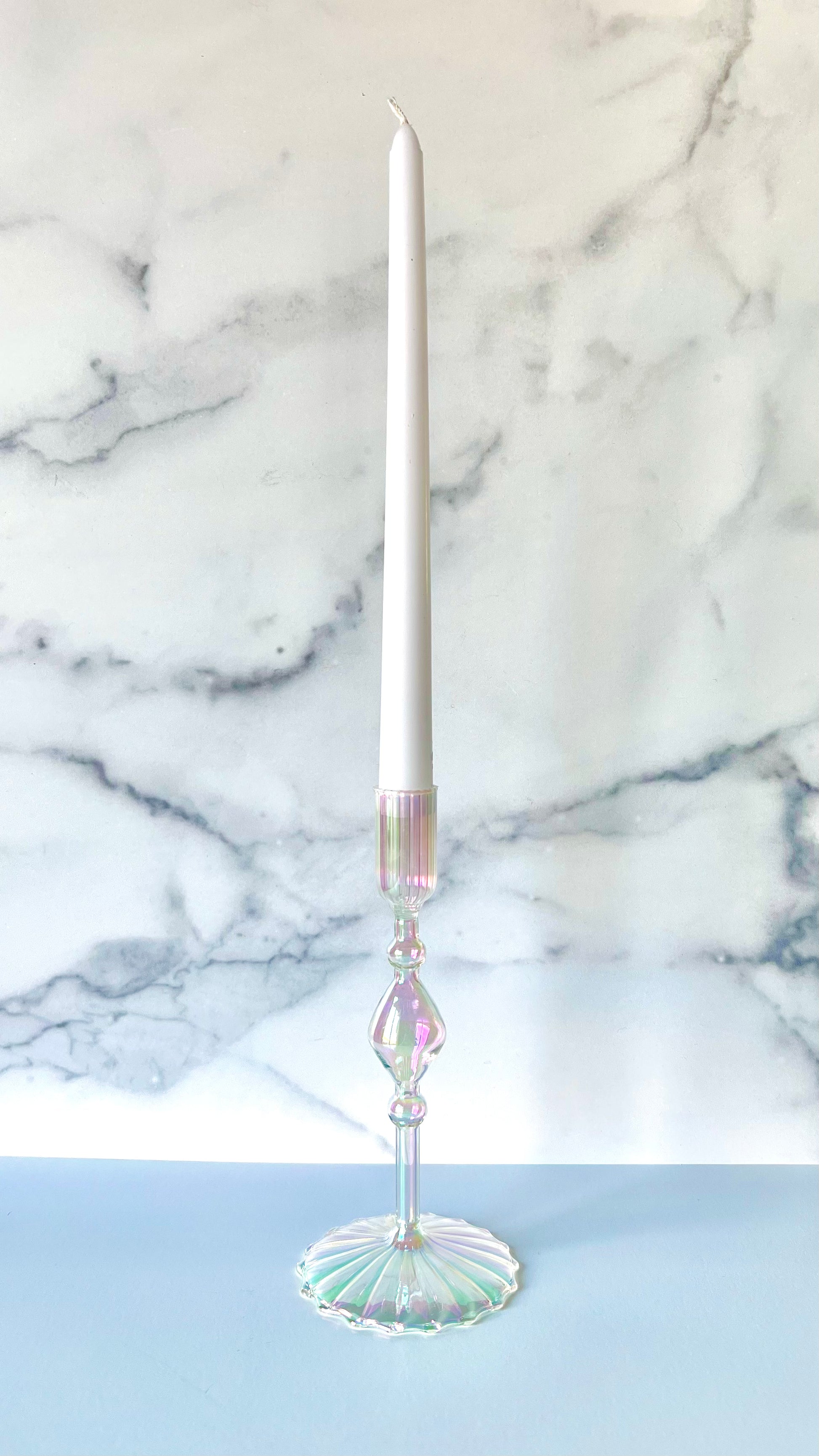 An iridescent glass candlestick with a white taper candle inside