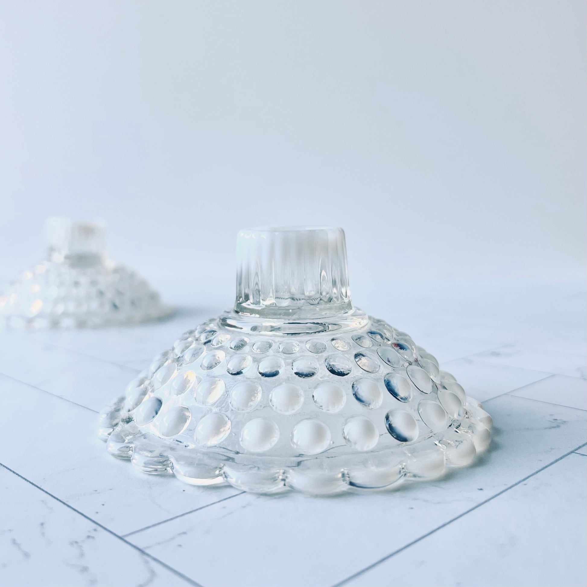 One white and clear hobnail candlestick with another in the background