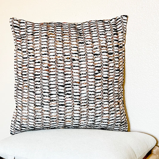 A white, brown and black textured square pillow against a light background