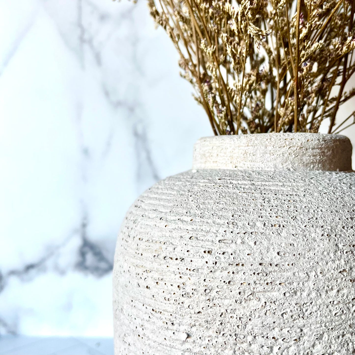 A close up of a gray striated vase showing its curves and large top opening, filled with dried stems