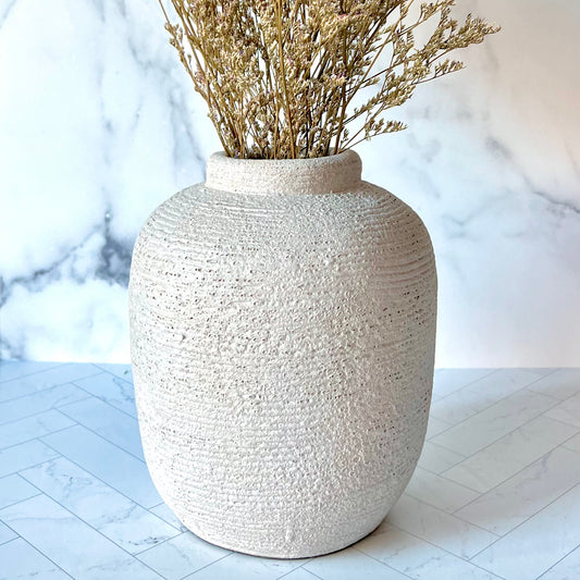 A gray vase on a white surface filled with dried flowers