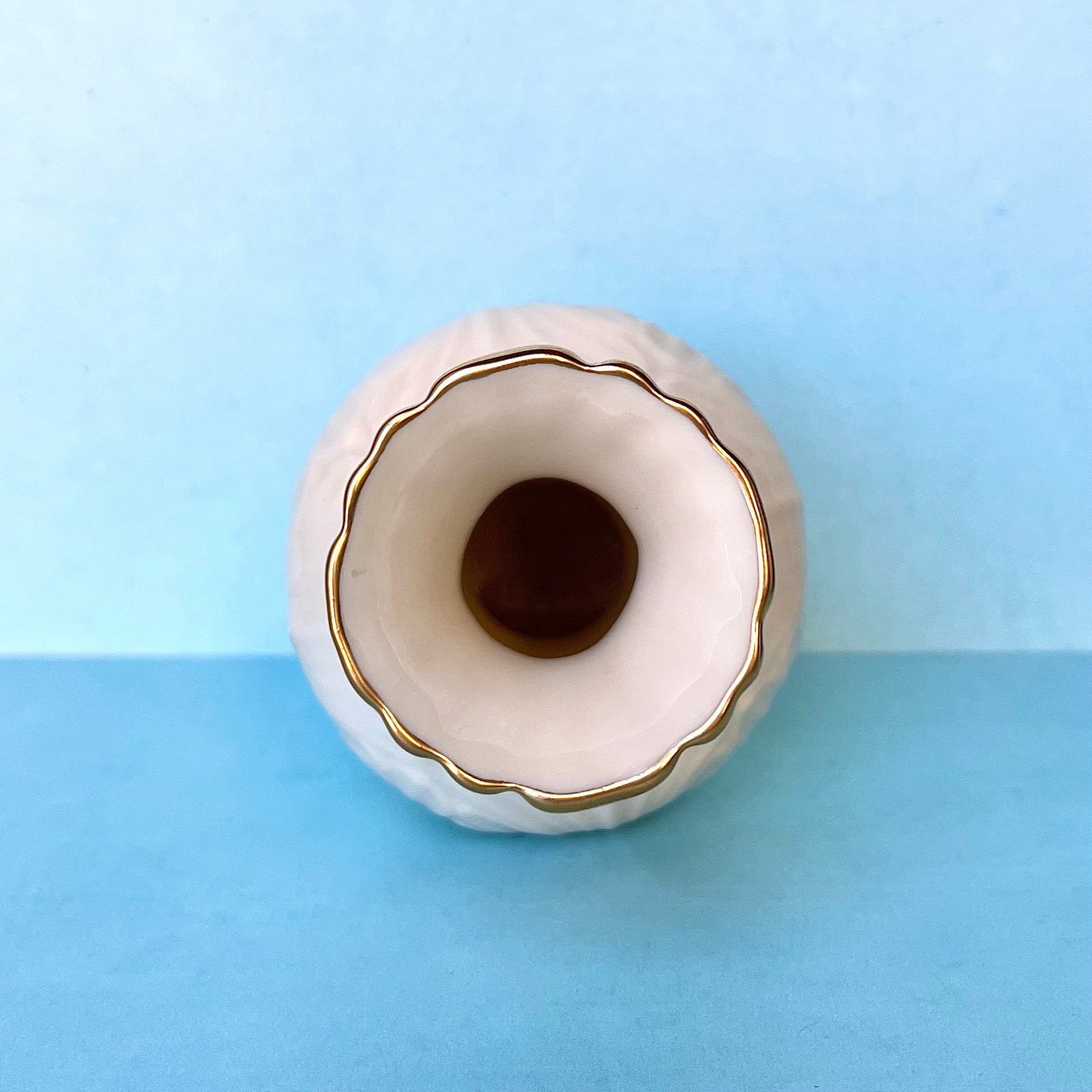 The top opening of a small white bud vase with gold trim