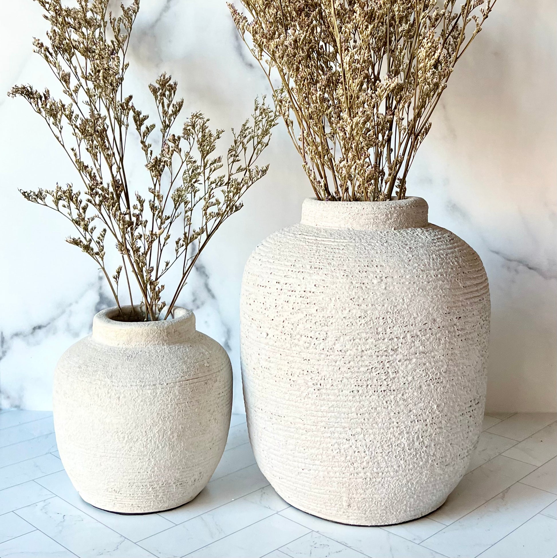 A large gray vase next to a small gray vase, both filled with dried flowers