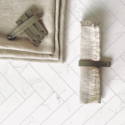 A Gray Leather Napkin Ring around a beige napkin with the other napkin rings on the side - The Offbeat Co.