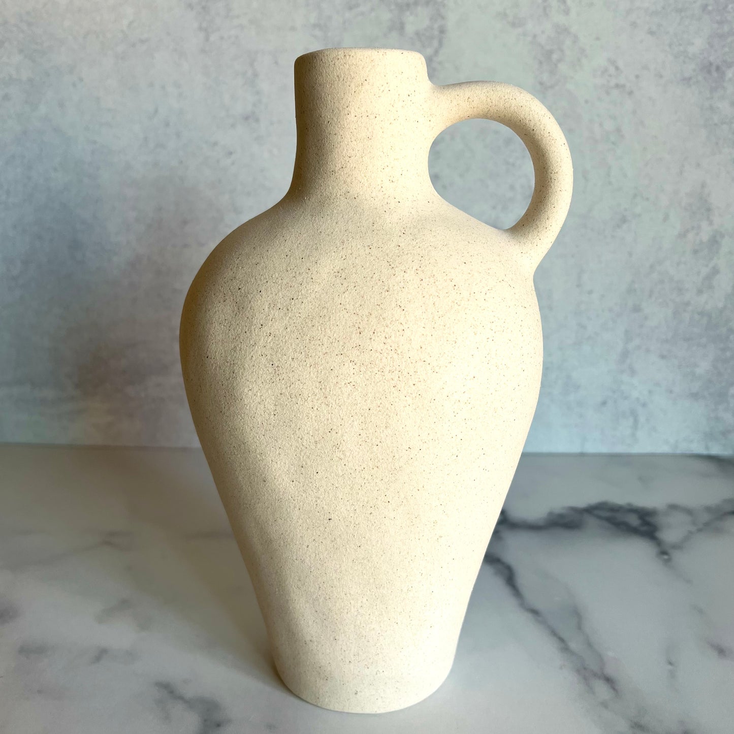 A beige vase with a small handle against a light gray background